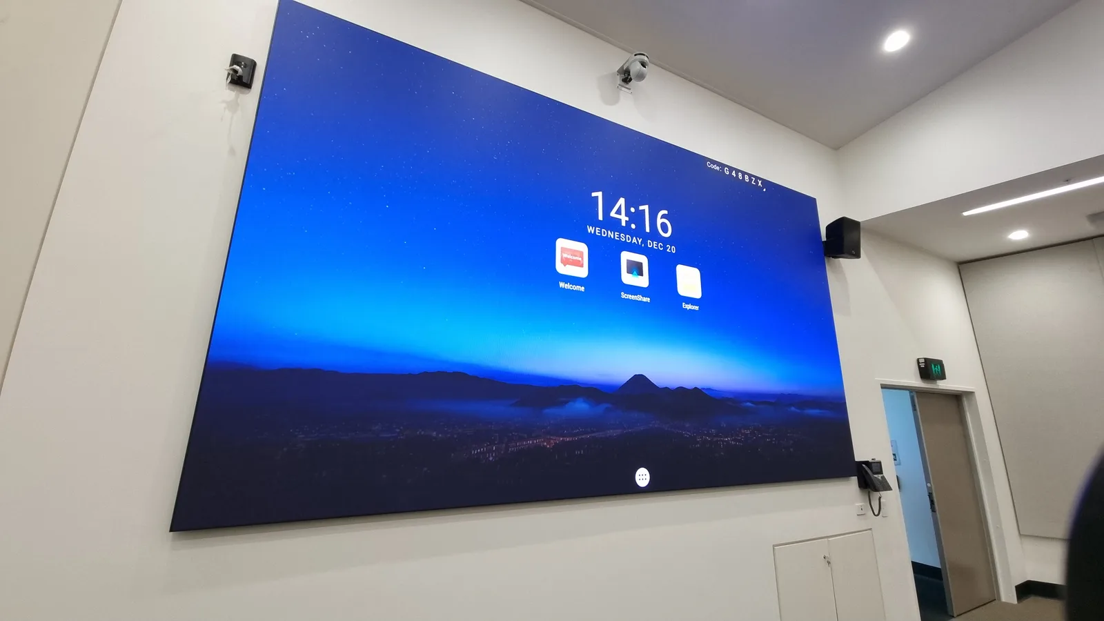 Aurora wall-mounted all-in-one LED conference display in a corporate function room showing a Welcome screen with date, time and ScreenShare/Explorer launchers