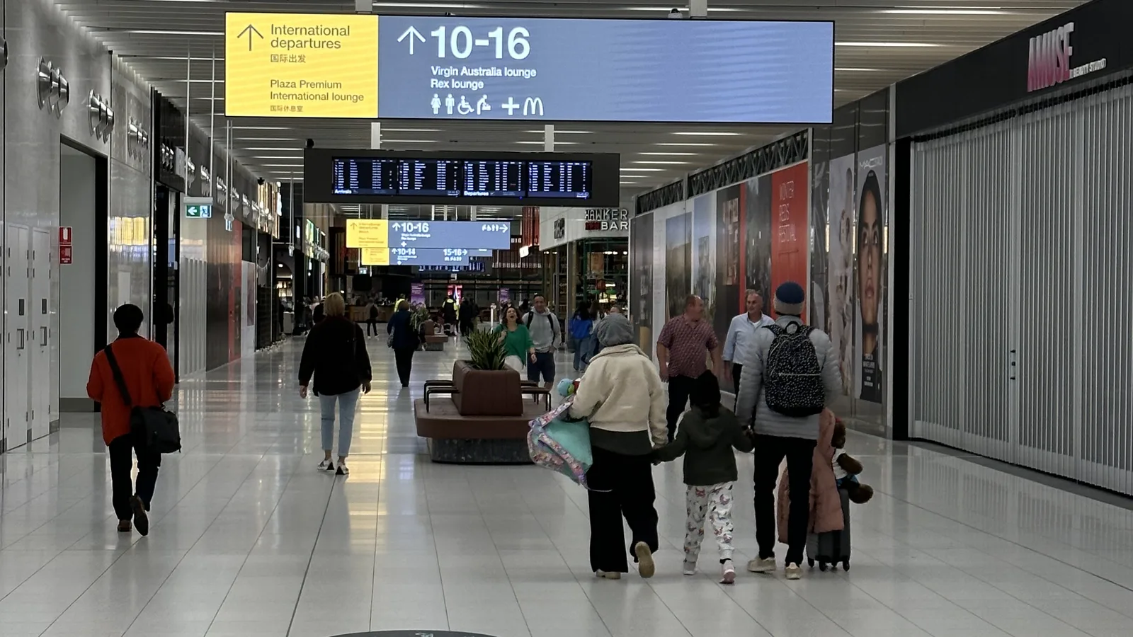 Aurora long-format LED wayfinding sign hanging in an Australian airport terminal showing departure gate ranges 10-16 above the concourse