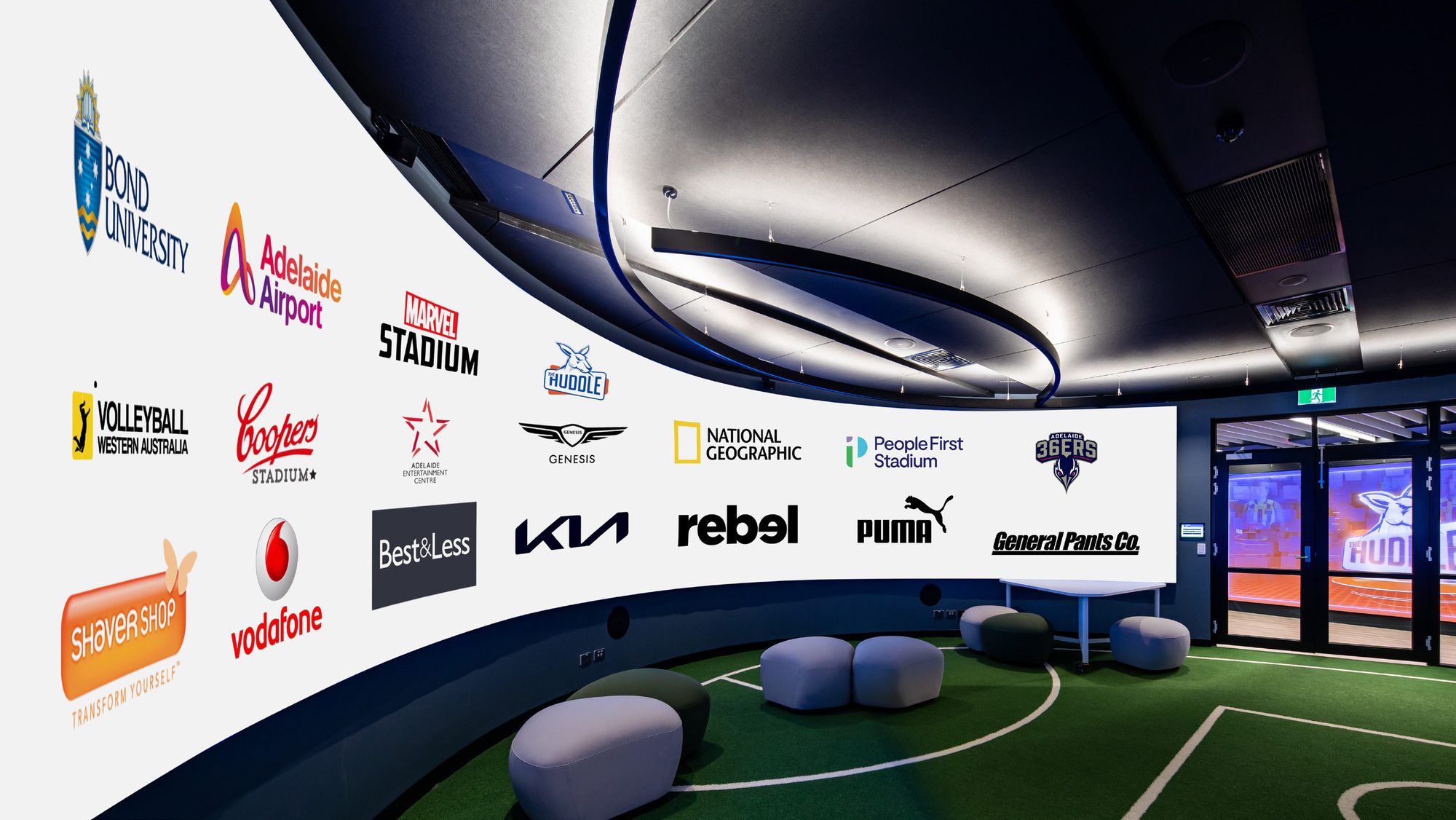 Curved LED feature wall in an Aurora showroom displaying client brand logos including Bond University, Adelaide Airport, Marvel Stadium, Genesis, National Geographic, People First Stadium, Adelaide 36ers, Puma, Rebel, Kia, Vodafone, Shaver Shop and Coopers Stadium